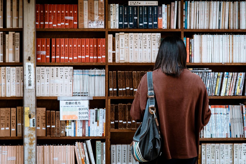 Estantería llena de libros en japonés y frente a ella una persona buscando un libro